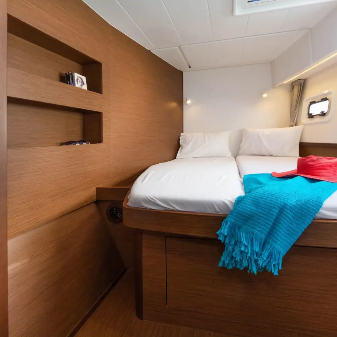 Double cabin of the Lagoon 42 with warm wood finish and hull window