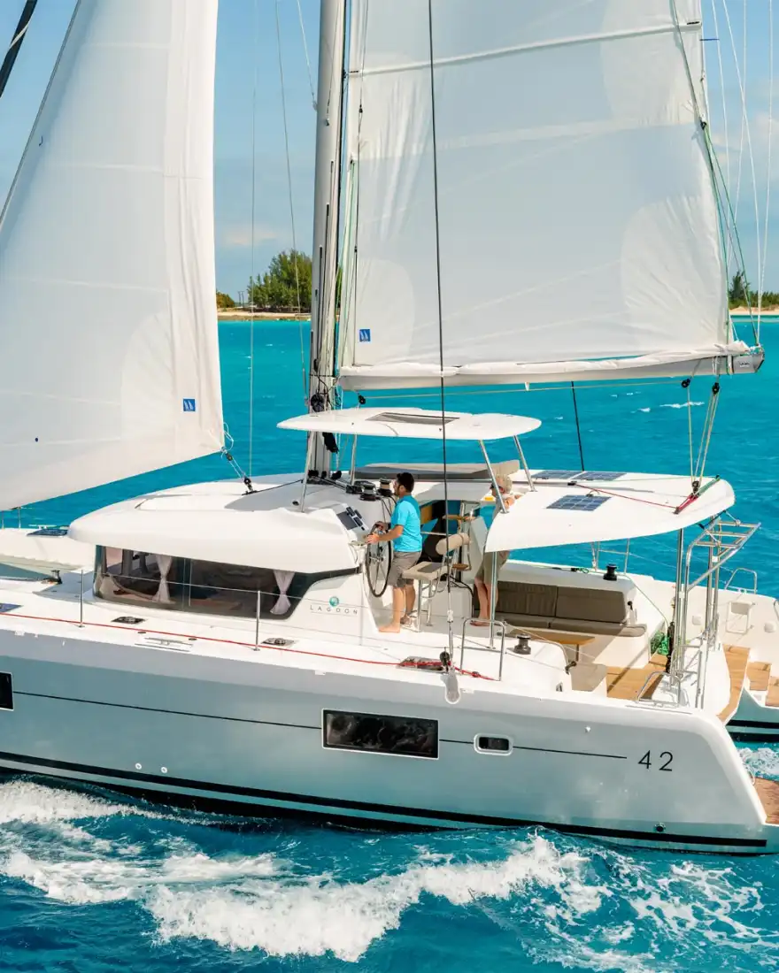 Lagoon 42 catamaran under full sail along a turquoise coastline